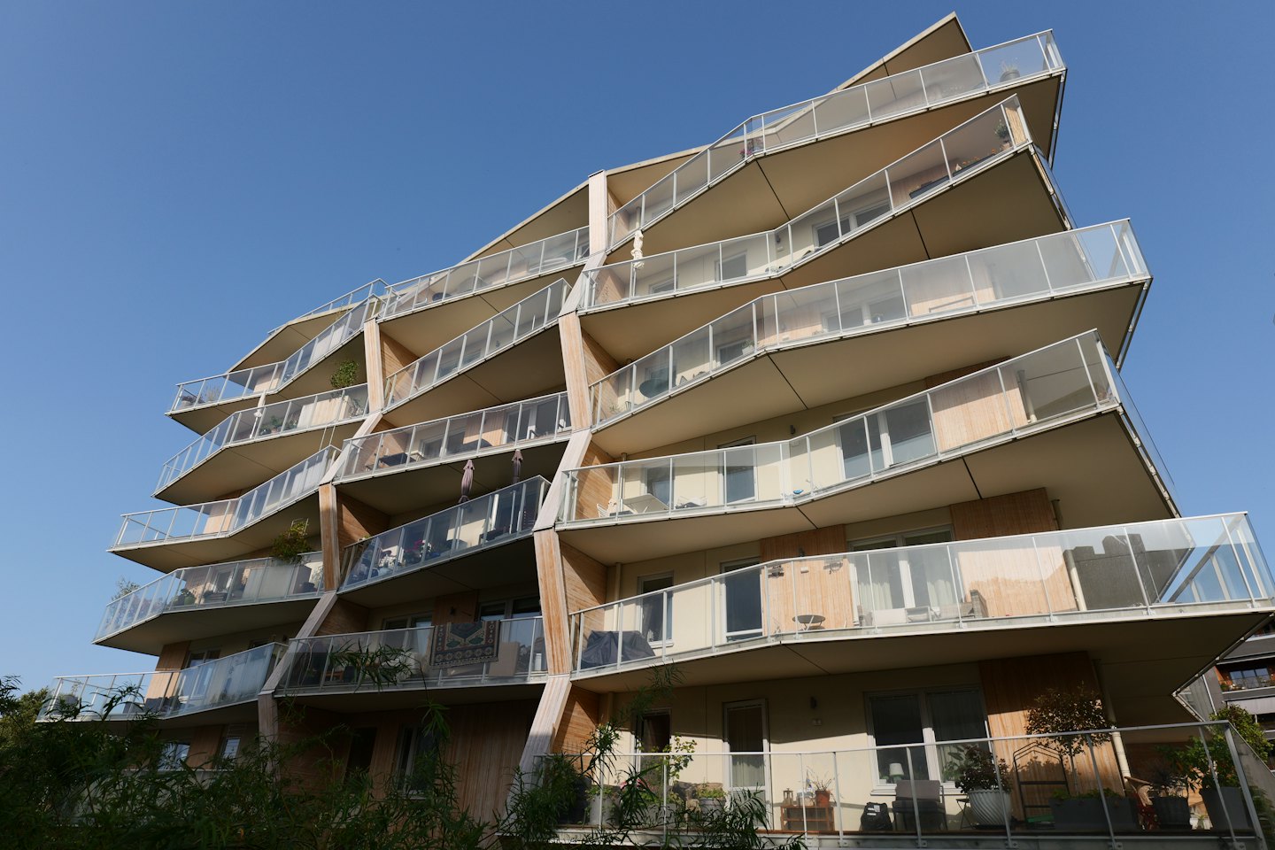 Modernes Wohnhaus mit geschwungenen Balkonen und Sitzgelegenheiten im Freien.